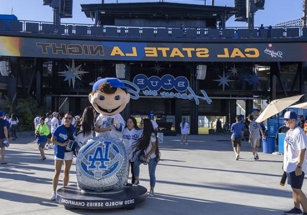 Group of alumni posing for photo with Bobblehead character at Dodger Stadium. 